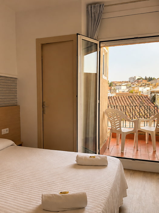 Habitación con camas individuales, ambiente cálido y luz natural junto a la ventana.